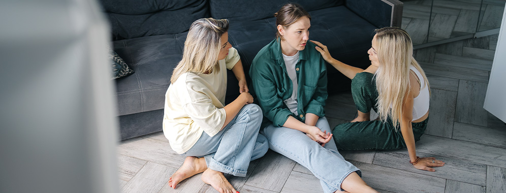 Drei Frauen sitzen vor einem Sofa auf dem Boden und reden miteinander.